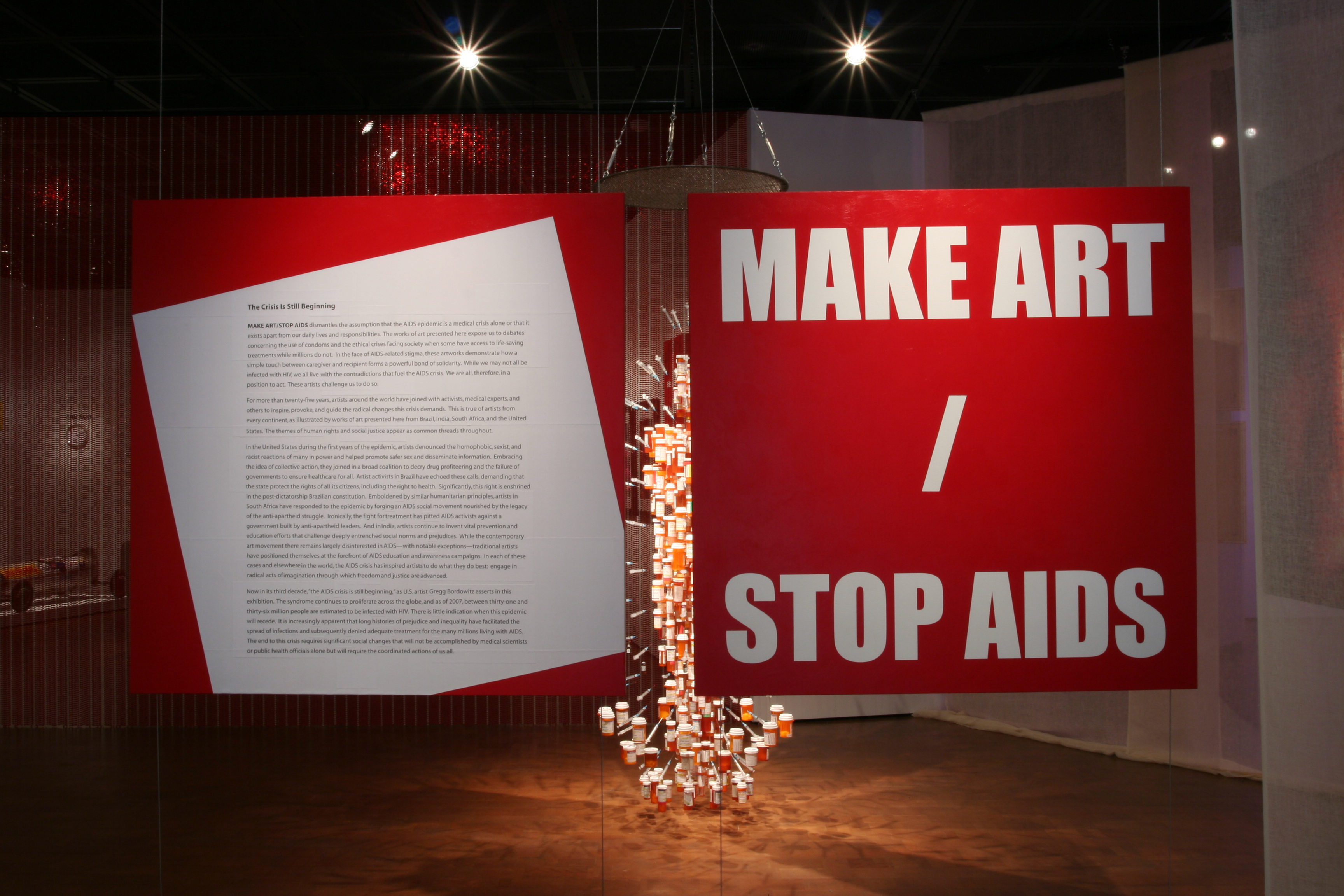 Large red MAKE ART/STOP AIDS title panel beside The Crisis Is Still Beginning introduction, with Medicine Man suspended between them