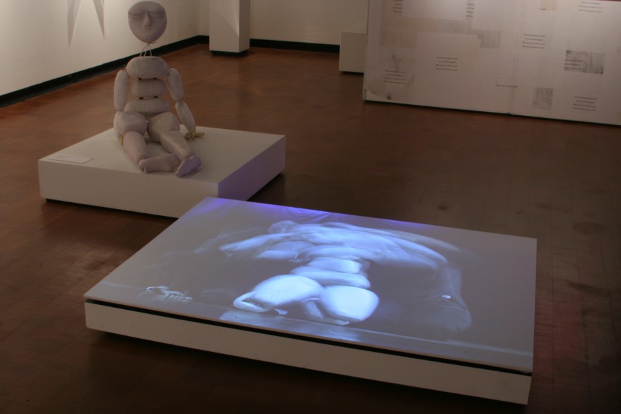 A puppet from *Virus ka Tamasha* sitting upright beside a projection of the video