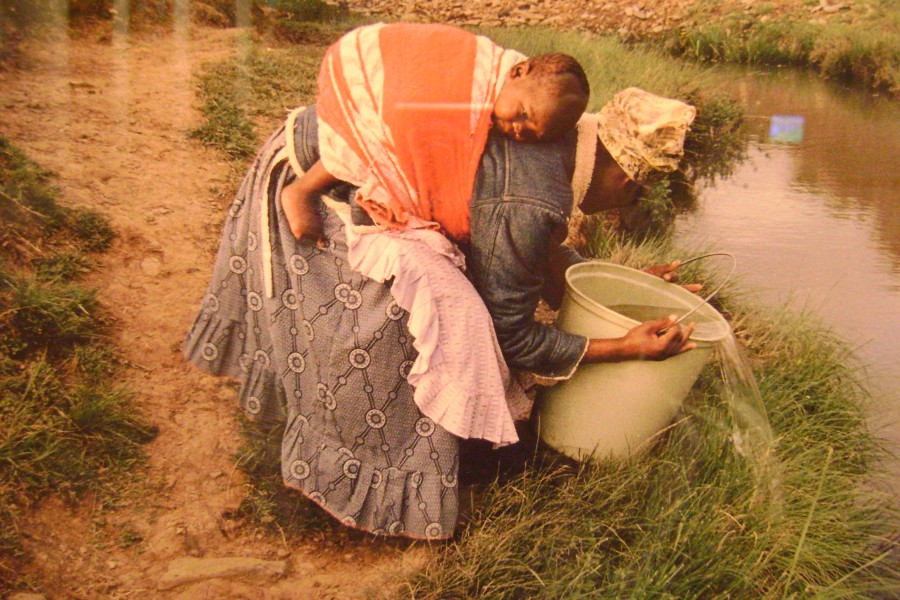Gideon Mendel’s photograph of Nozamile Ndarah carrying water with a sleeping child on her back