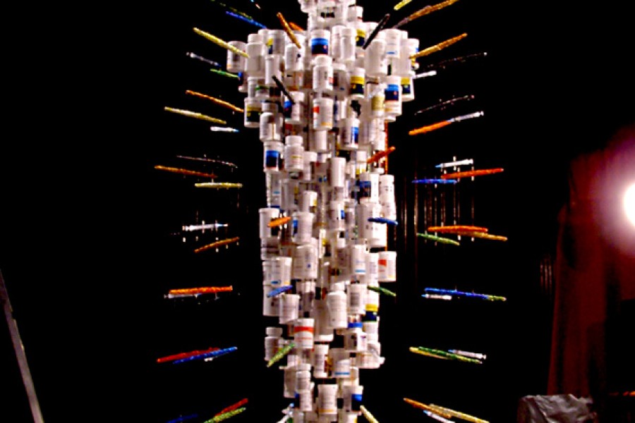 Full view of a version of *Medicine Man*, a suspended human figure made from HIV medication bottles and radiating syringes above a labeled circular base