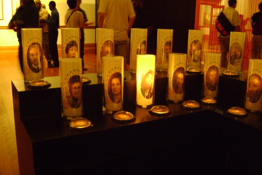 Candles bearing portraits in Jean Carlomusto’s *Offerings*