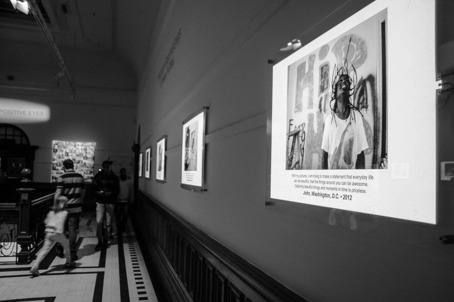 Visitors walking past and viewing photographs and first-person biographical statements during the exhibition opening