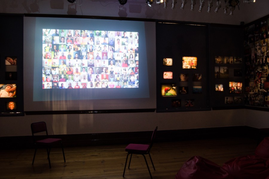 Gideon Mendel’s grid of artivist portraits projected in the empty Banishing Stigma Room, with photographic prints spotlit on adjacent walls