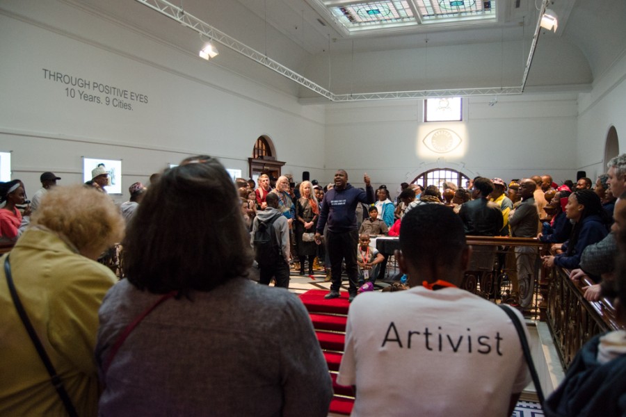 Person speaking before a large crowd at the exhibition opening
