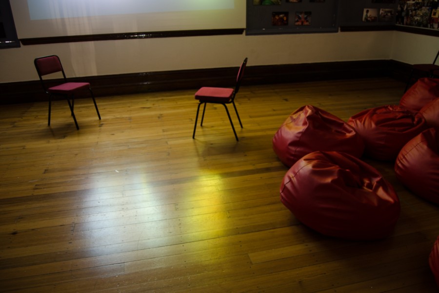 Red beanbag audience seating facing two chairs on a stage and a projector screen