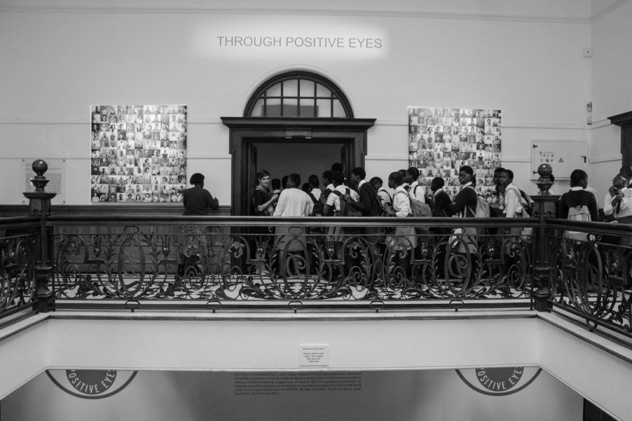 Crowd filing into a second-floor gallery through an entrance flanked by portrait grids