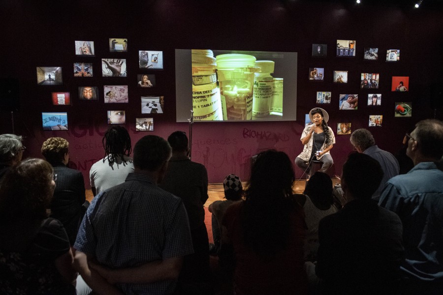 Porchia storytelling before an audience in the Banishing Stigma Room with one of her photographs projected behind her