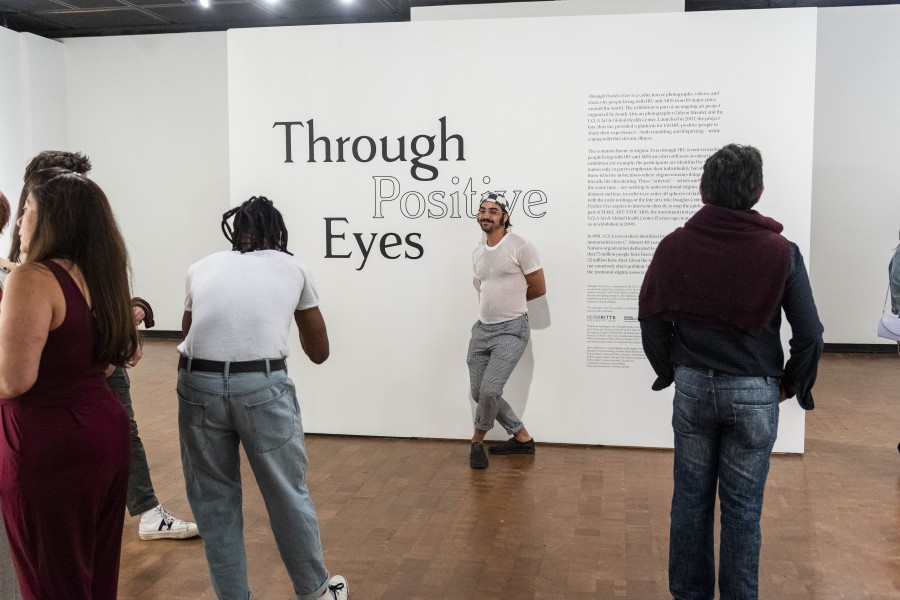 Vas posing in front of introductory text on the Through Positive Eyes title wall