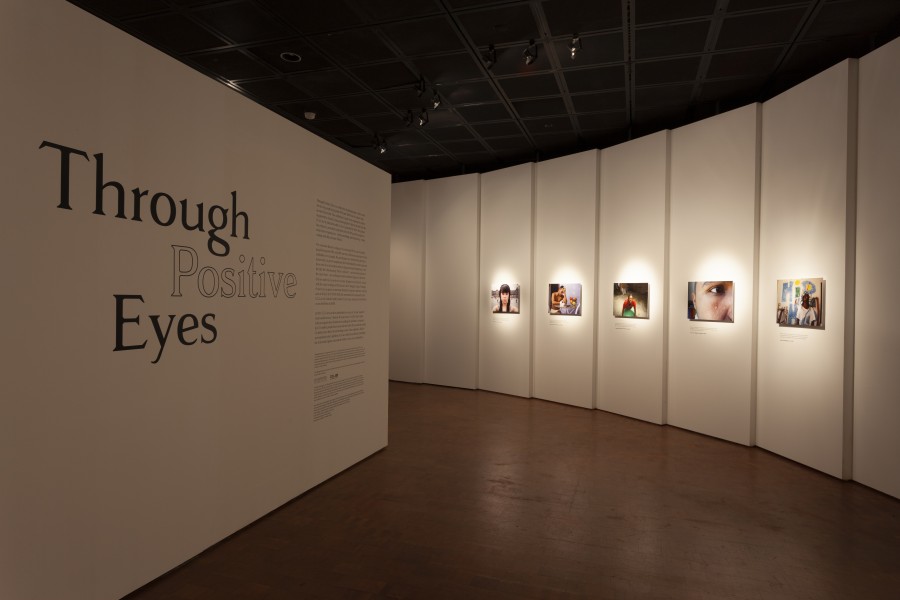 Gallery view with the Through Positive Eyes title wall, introductory text, and artivist photographs