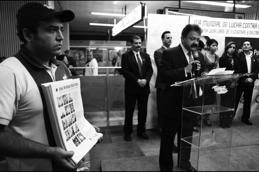 One person speaking while another holds portraits of the 14 Through Positive Eyes artivists